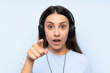 Young woman listening music over isolated blue background surprised and pointing front