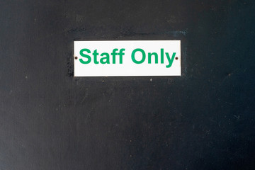 STAFF ONLY signage on a wooden door, black background,