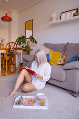 Musician woman trying to compose a creative song. Creative person, design, music and arts lifestyle. Young woman doing homework and sitting on floor writing creative ideas on a red notebook at home.