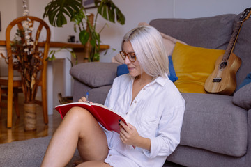 Hipster woman with white dyed hair and creative mind exploring and writing new ideas on notebook. Side view portrait of young businesswoman in her workplace, writing down some information.