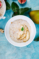 Healthy breakfast. A bowl of porridge with pears slices and walnuts on blue background.  Flat lay. Copy space. Top view.