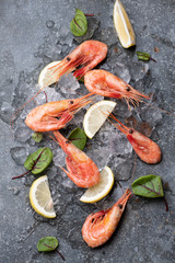 Bright juicy shrimps on ice with lemon, green leaves.
