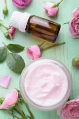 Homemade creame and essential oil with roses on wooden background.