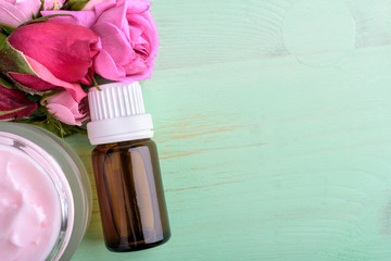 Homemade creame and essential oil with roses on wooden background.