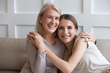 Happy elderly mother and adult daughter holding hands embracing indoors