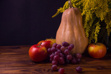 pumpkin apples grapes and yellow flowers on a black background on a wooden table. It looks like a still life