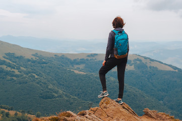 Naklejka premium Young girl tourist with backpack behind her stands on top of the mountain and enjoys a view of the Carpathian mountains at sunrise.