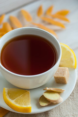 white cup of tea with lemon, ginger and brown sugar on the wooden table with autumn leaves