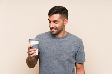 Handsome man with beard holding a take away coffee over isolated background smiling a lot