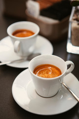 Close up. The small white ceramic mug (cup) with Italian espresso (coffee) on a table with a saucer and a metal spoon in a local Italian bar (coffee shop) in Milan, Lombardy, Italy. Beverage.