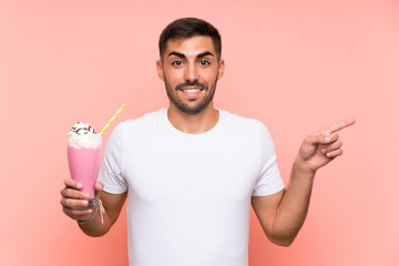 Young man with strawberry milkshake over isolated pink background surprised and pointing finger to the side
