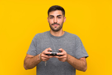 Young handsome man playing with a video game controller over isolated yellow background