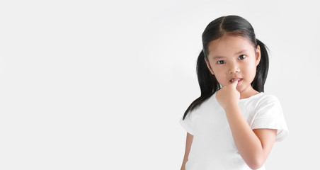Asian child cute or kid girl nail biting on finger and smiling with anxious or thinking enjoy on preschool or 5 years old and wear white T-shirt and white background isolated with copy space
