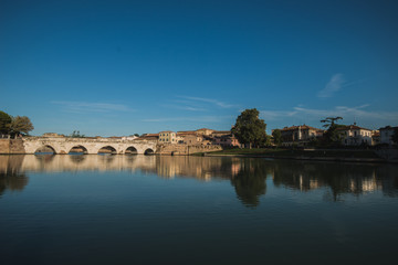 Obraz premium Rimini, Italy - September 11, 2019: Tiberius bridge in Rimini on a background of blue sky with white clouds