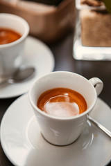 Close up. The small white ceramic mug (cup) with Italian espresso (coffee) on a table with a saucer and a metal spoon in a local Italian bar (coffee shop) in Milan, Lombardy, Italy. Beverage.
