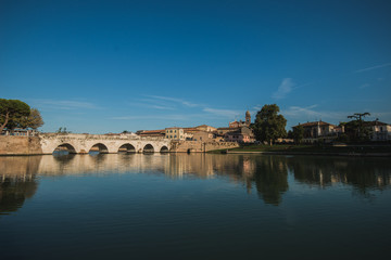 Fototapeta premium Rimini, Italy - September 11, 2019: Tiberius bridge in Rimini on a background of blue sky with white clouds