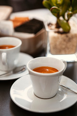 Close up. The small white ceramic mug (cup) with Italian espresso (coffee) on a table with a saucer and a metal spoon in a local Italian bar (coffee shop) in Milan, Lombardy, Italy. Beverage.