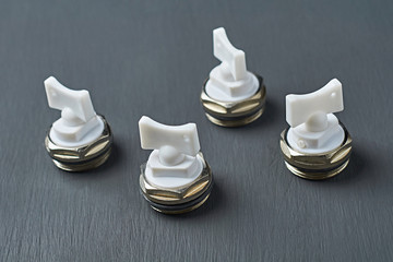 Four metal air valves with white plastic handle for to vent excess air and pressure from heater radiator in room lies on dark scratched desk in workshop. Close-up