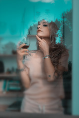 ragazza dietro la finestra con un calice di vino in mano