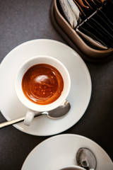 Close up. The small white ceramic mug (cup) with Italian espresso (coffee) on a table with a saucer and a metal spoon in a local Italian bar (coffee shop) in Milan, Lombardy, Italy. Beverage.