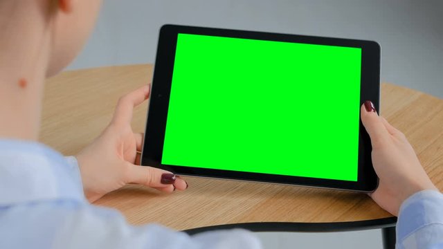 Mock up, freelance, copyspace, template, leisure time, green screen, technology concept - woman sitting at wooden table and looking at black digital tablet computer device with blank green display