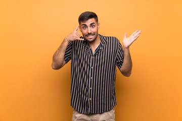 Handsome man with beard over isolated background making phone gesture and doubting