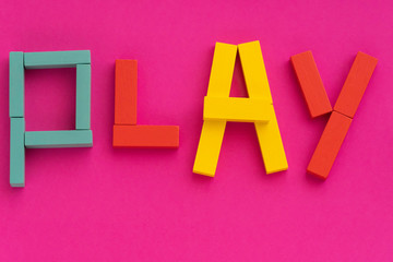 Word PLAY made from multicolored wooden bricks toys on purple paper background. Kids game concept. Bright colors of red, yellow, blue on a pink background. Top view, flat lay