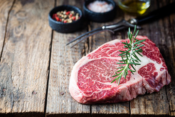 Raw fresh meat Ribeye Steak and seasonings on wooden background, rustic style