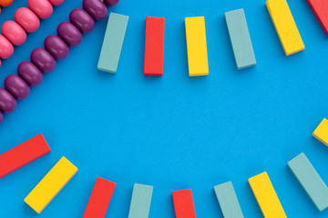 Frame from kids toys, top view on children's educational games on blue paper background. Multicolored wooden bricks, abacus. Flat lay, copy space for text