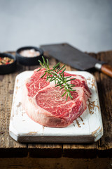 Raw fresh meat Ribeye Steak and seasonings on wooden background, rustic style