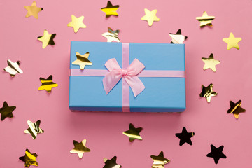 top view beautiful blue gift box with pink satin ribbon with bow on a pink background with golden stars sequins