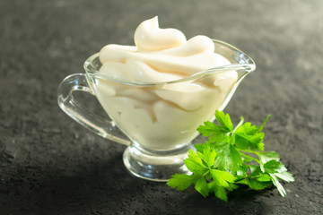  Mayonnaise in a sauceboat and a bunch of parsley on a black background.