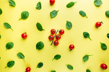 Spinach leaves and tomato pattern background on yellow, top view