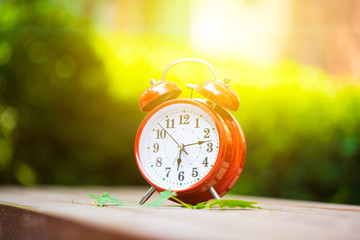 Morning concept. Alarm clock closeup. Red alarm clock on garden table with natural lights background, outdoors