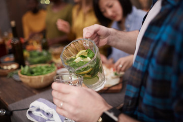 Closeup of unrecognizable young man pouring refreshing lemonade into glass while enjoying Summer party with friends, copy space