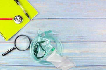 Top view of medical oxygen face mask, stethoscope, file, pen and magnifying glass on wooden...
