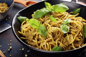 Plate of delicious spaghetti pesto garnished with parmesan cheese and basil on rustic dark background