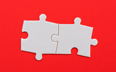 Puzzle pieces on red background, two, close up.