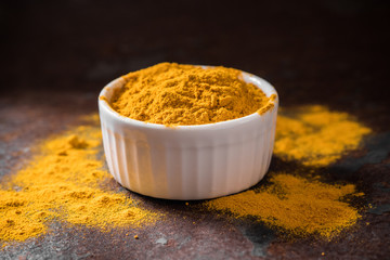 Turmeric powder. Traditional indian golden healthy spice in white ceramic bowl on dark background