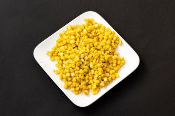 Boiled corn on a white plate. Black background. Top view.