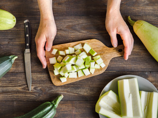 Zucchini harvest. Woman slices zucchini cubes for freezing on wooden table. Farm organic zucchini...