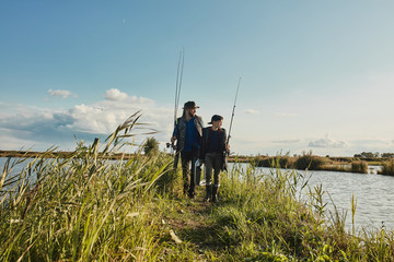 Caucasian father and son walk on islet among lake. They choose good place for fishing together to...