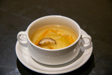 A clear soup in a white cup