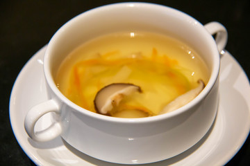 A clear soup in a white cup
