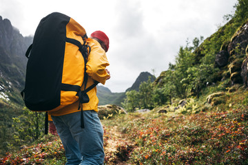 Tourist with backpack standing in front of the mountain massif while journey by scandinavian. Male traveler wearing yellow jacket explore national park and hiking outdoor landscape