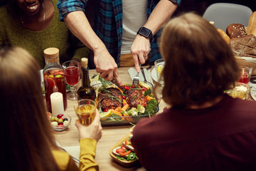 Close up of unrecognizable people enjoying dinner together, focus on man cutting delicious meat loaf set on wooden table, copy space