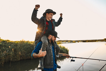 Father and son have fun while fishing. Teen boy happy and smile, sit on father shoulders and raised...