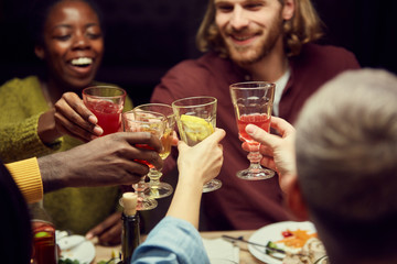 Cropped photo of young friends clinking glasses with colorful alcohol while enjoying party in dark room, copy space