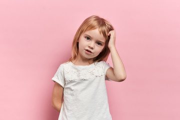 serious girl scratching her head. Uncertain with doubt, thinking with hand on head. little girl making up a plan, solve, overcome problem, close up portrait, isolated pink backgorund, studio shot