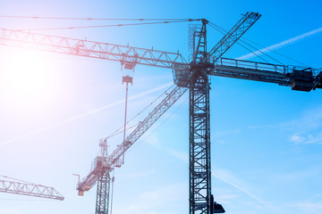 Big tower cranes against the blue sky. Background image of construction equipment close-up with copy space.